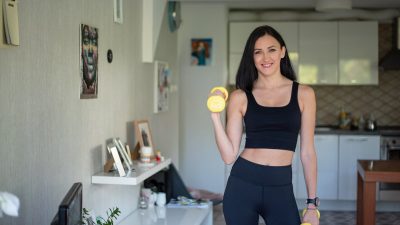 Smiling woman in activewear lifting dumbbells at home for a healthy lifestyle.